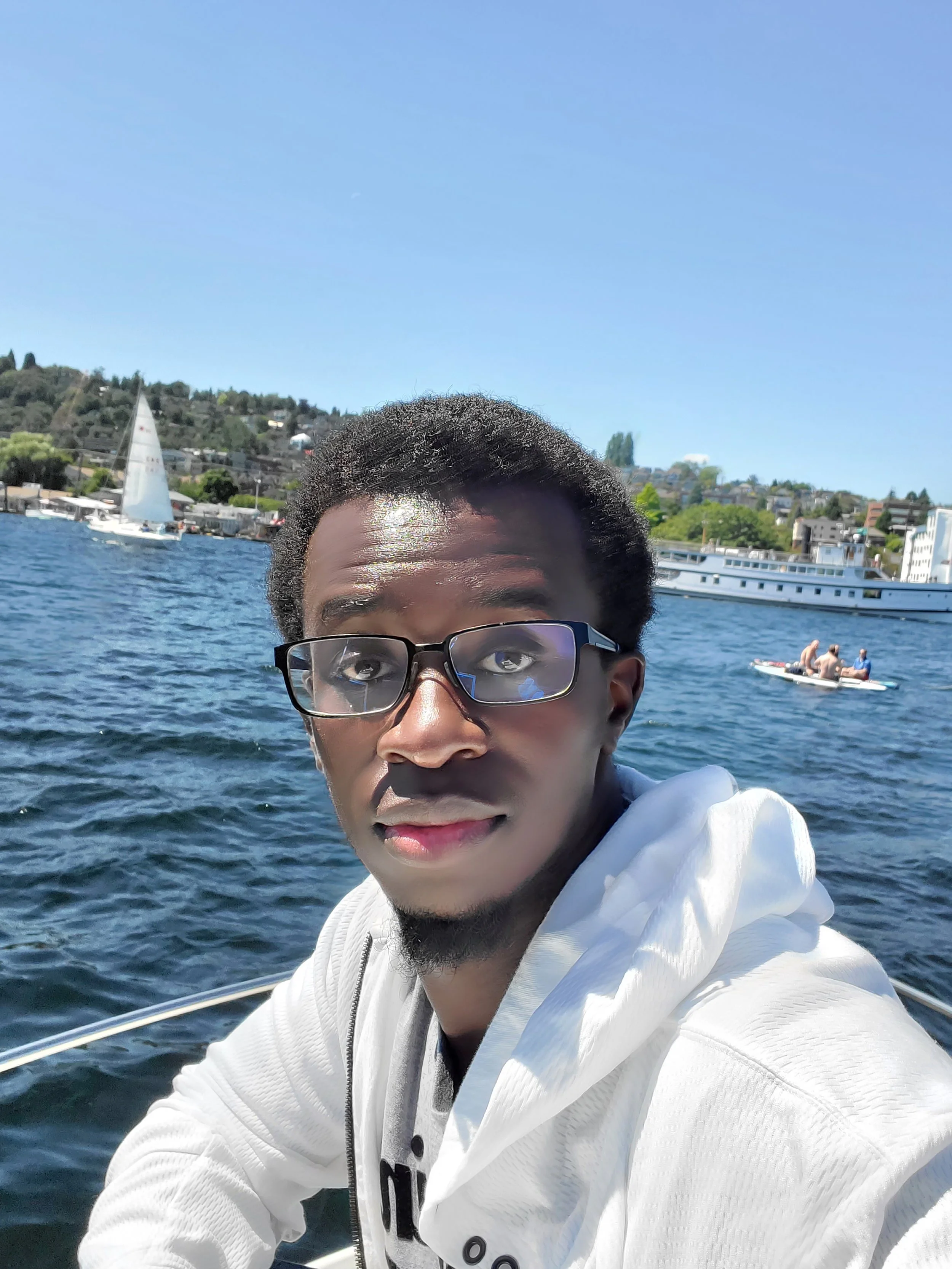 Author, Cedric Strickland, wearing glasses and a white hoodie on a boat with a lake and sailboats in the background.